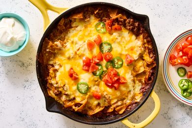 Beef enchilada skillet topped with melted cheese, chopped tomatoes, and jalapenos