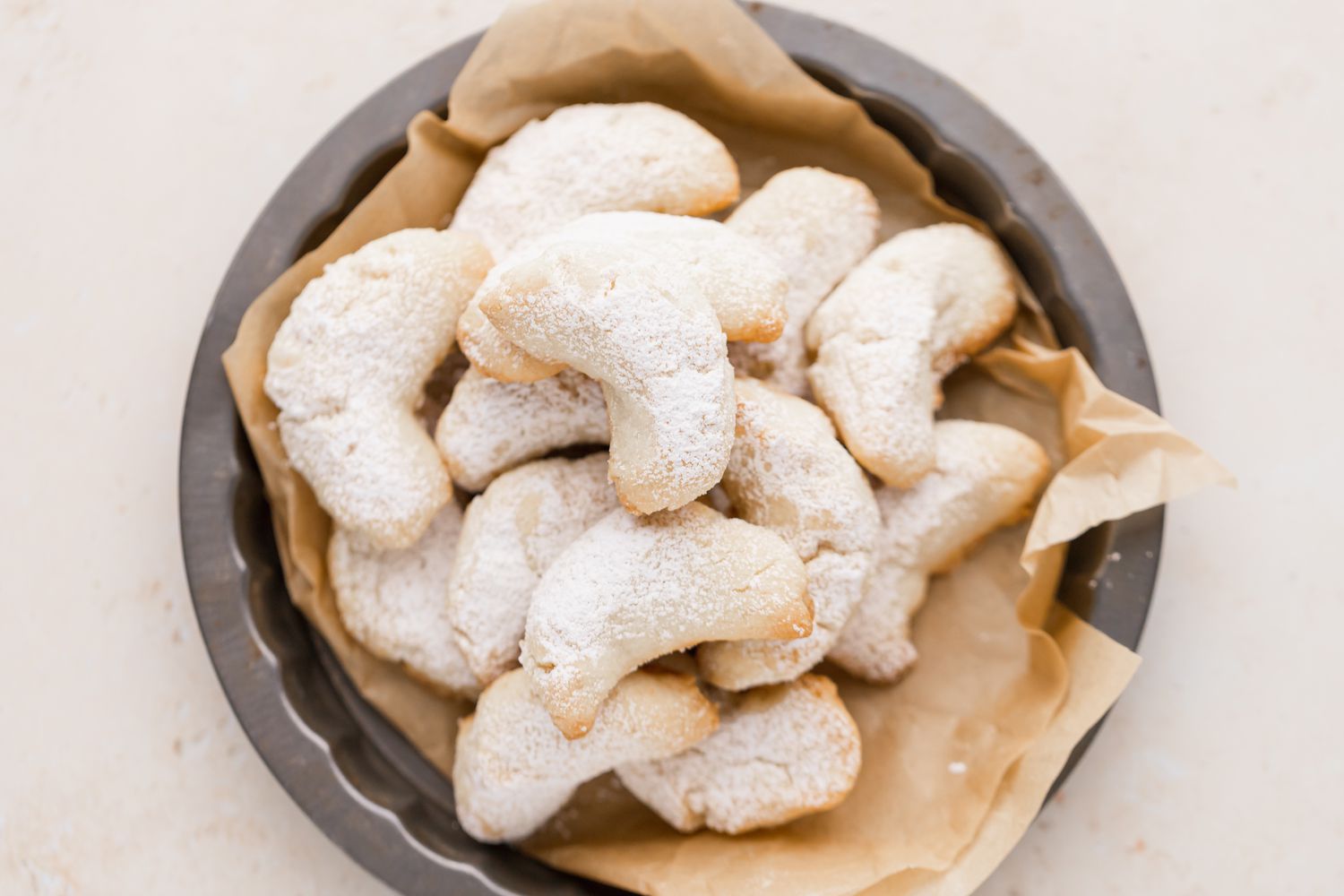 Overhead view of almond crescent cookies on a parchment lined decorative baking pan.