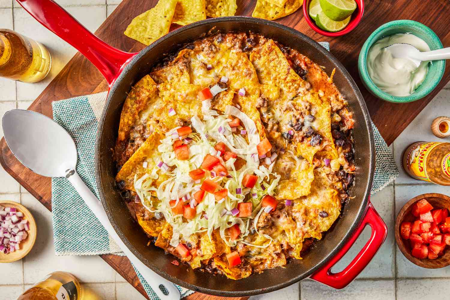 easy taco casserol in a pot at a table setting with bowls of toppings, chips on a platter, and a bottle of beer