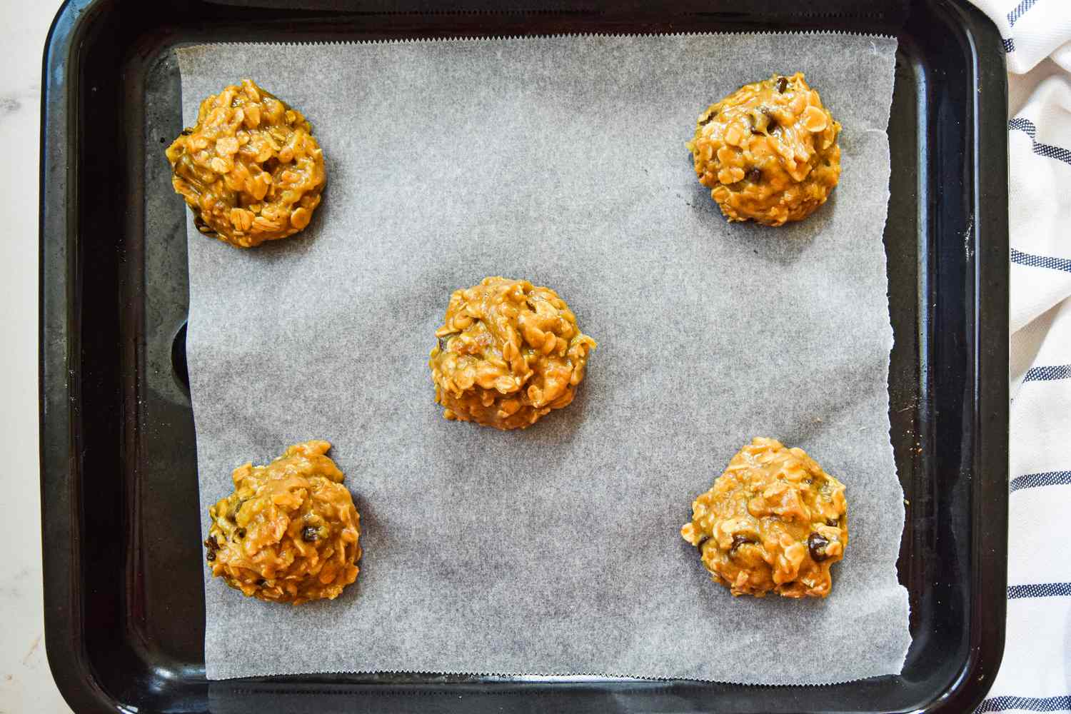 Portions of Oatmeal Banana Cookie Batter on a Parchment Paper Lined Baking Pan