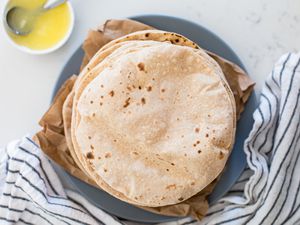Overhead view of a stack of Indian flatbread roti on a plate with a striped linen underneath.