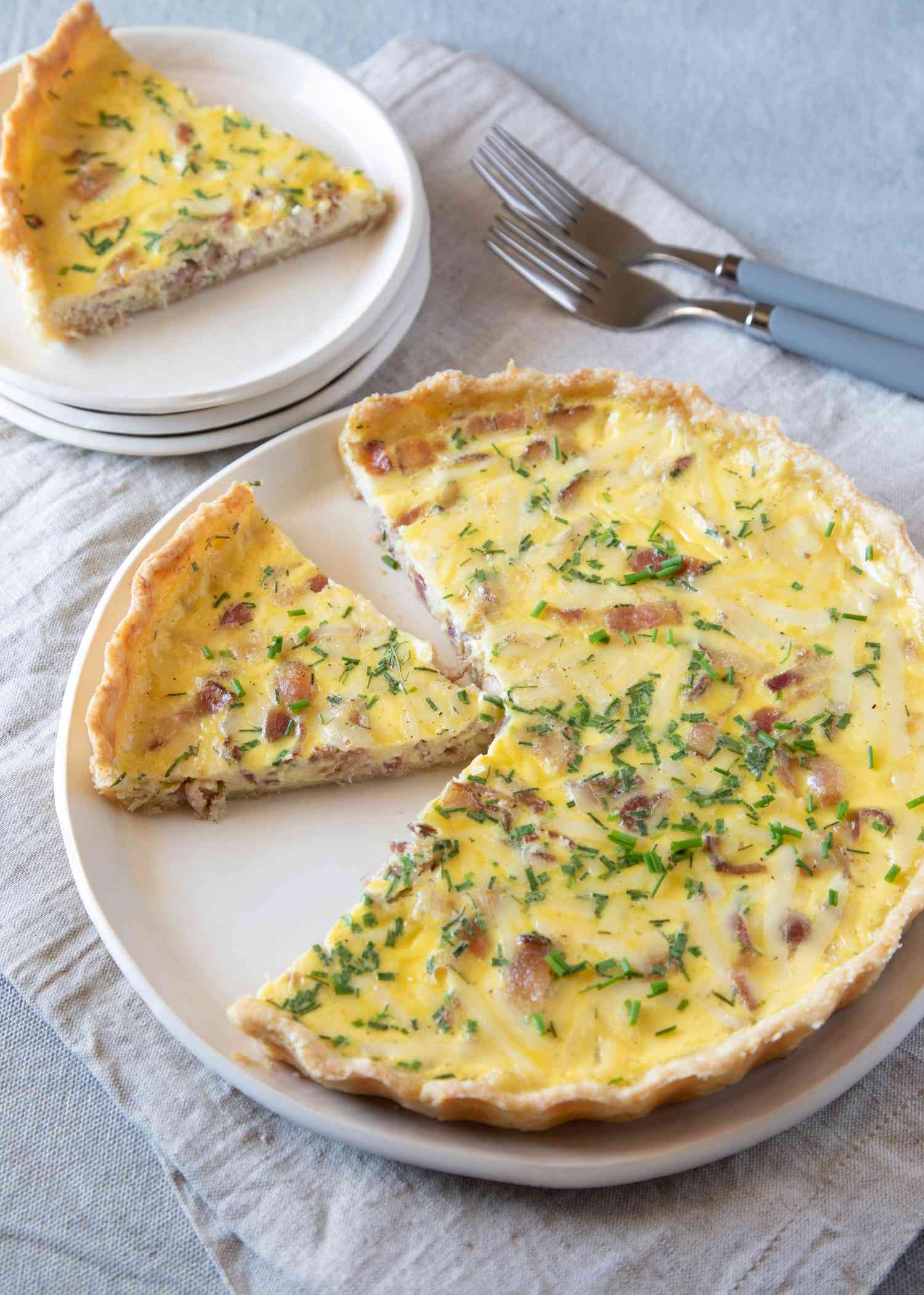 Quiche lorraine with a piece set on a plate behind it.