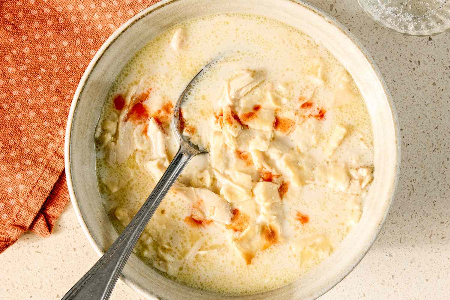 A bowl of creamy chicken mull soup with a spoon garnished with a sprinkle of red seasoning