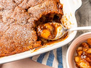 A pear pudding cake in a baking dish with a spoon serving a portion showcasing a dessert with fruit filling
