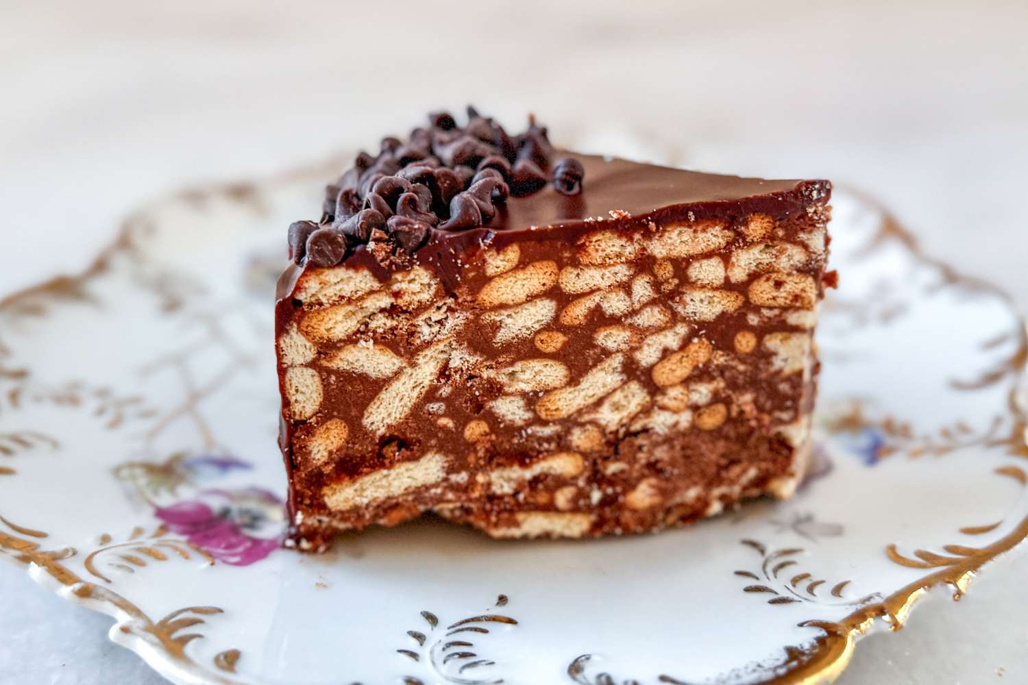A slice of chocolate biscuit cake topped with chocolate pieces displayed on a decorative plate