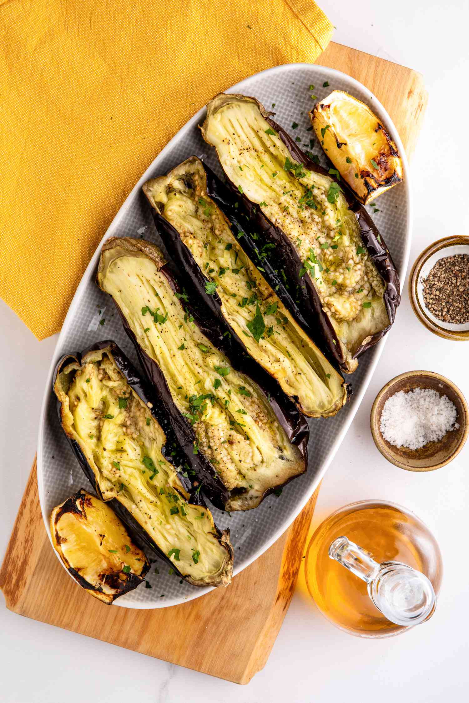 Platter of Whole Grilled Eggplant Surrounded by Bowls of Salt and Pepper