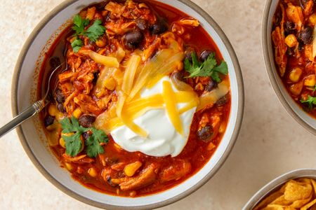 Bowl of chili with shredded chicken topped with sour cream and cheese and garnished with cilantro