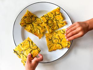 two hands taking pieces of Tuscan zucchini scarpaccia from a plate