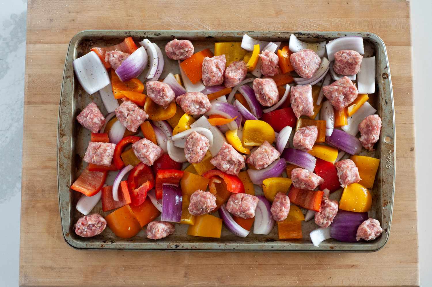 Sheet pan sausage dinner on a wooden block ready for the oven.