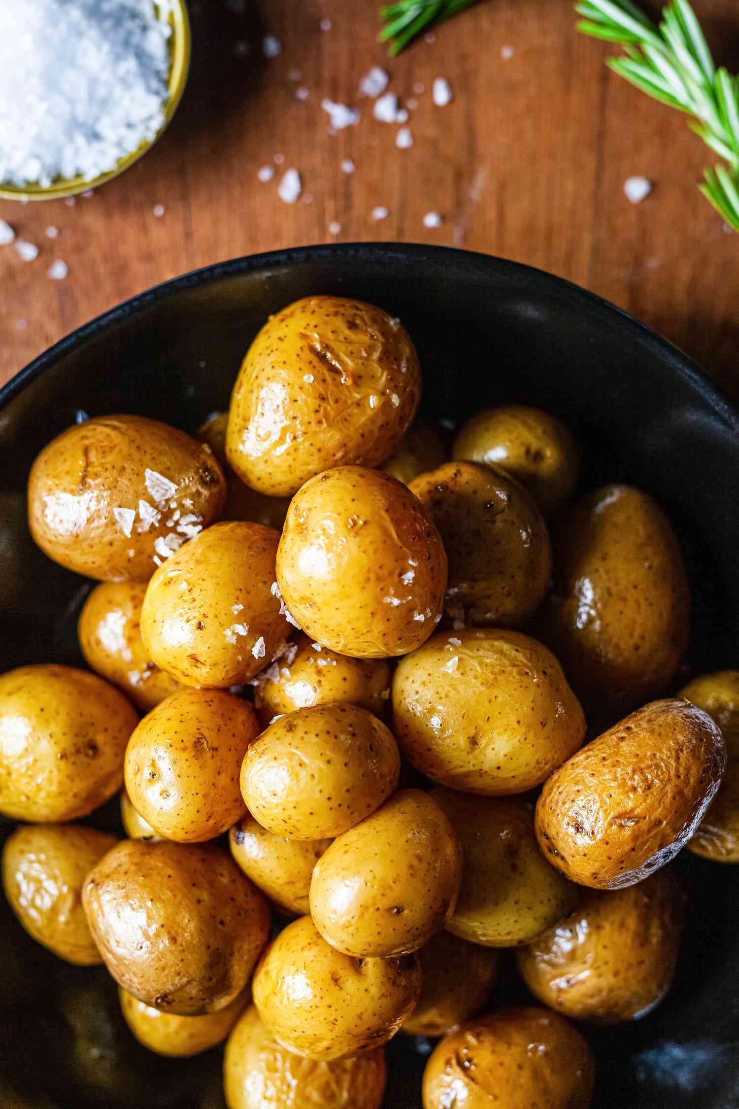 Potato confit on black platter with salt and rosemary.