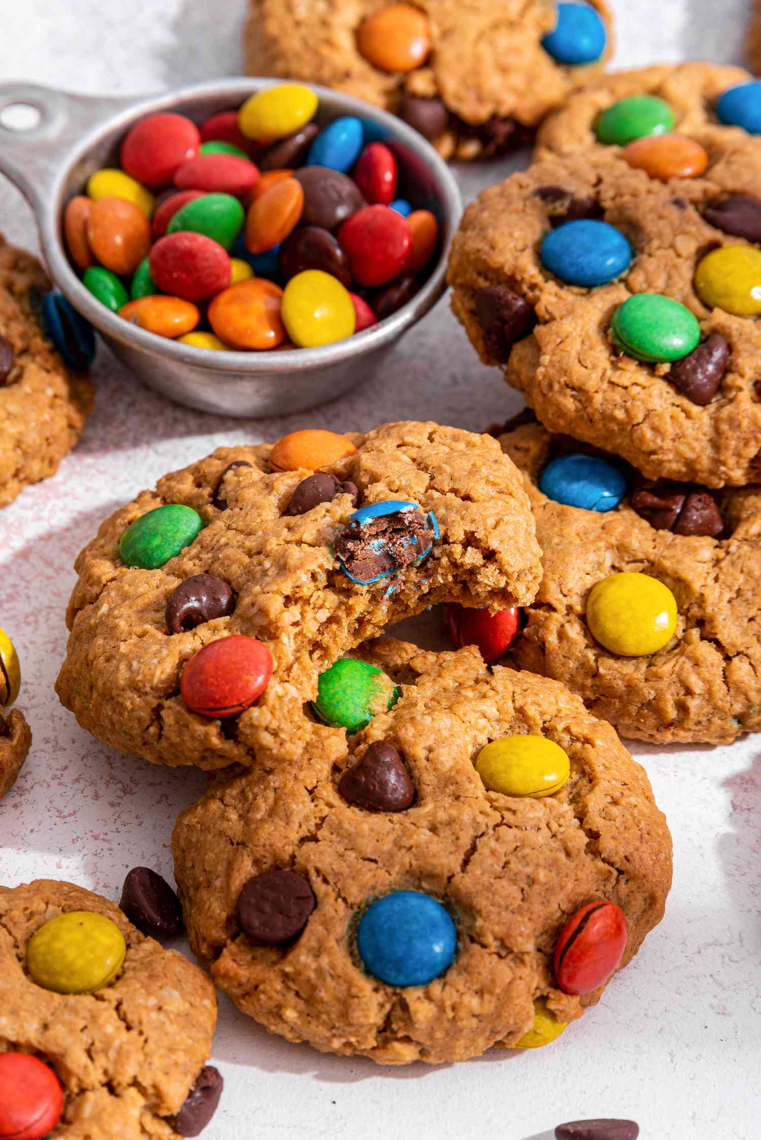 Monster cookies on the counter with one cookie bitten into and a small bowl of M&M's 