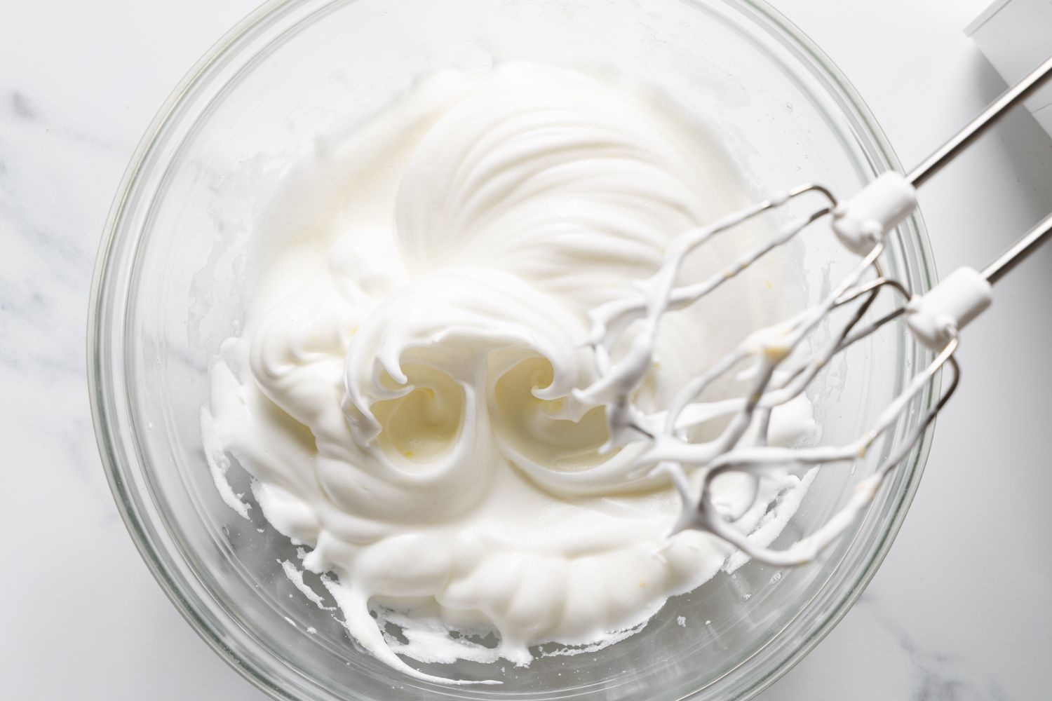 Overhead view of a clear glass bowl with beaters from a mixer and egg whites after beating for Magic Lemon Pie recipe 