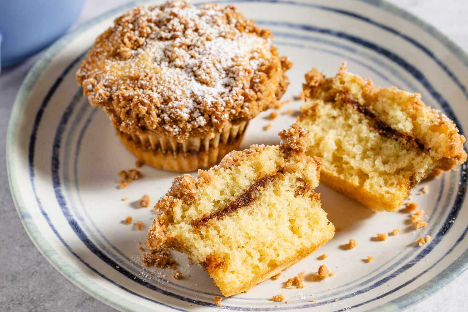 A coffee cake muffin on a plate with one muffin cut to show the cinnamon swirl inside