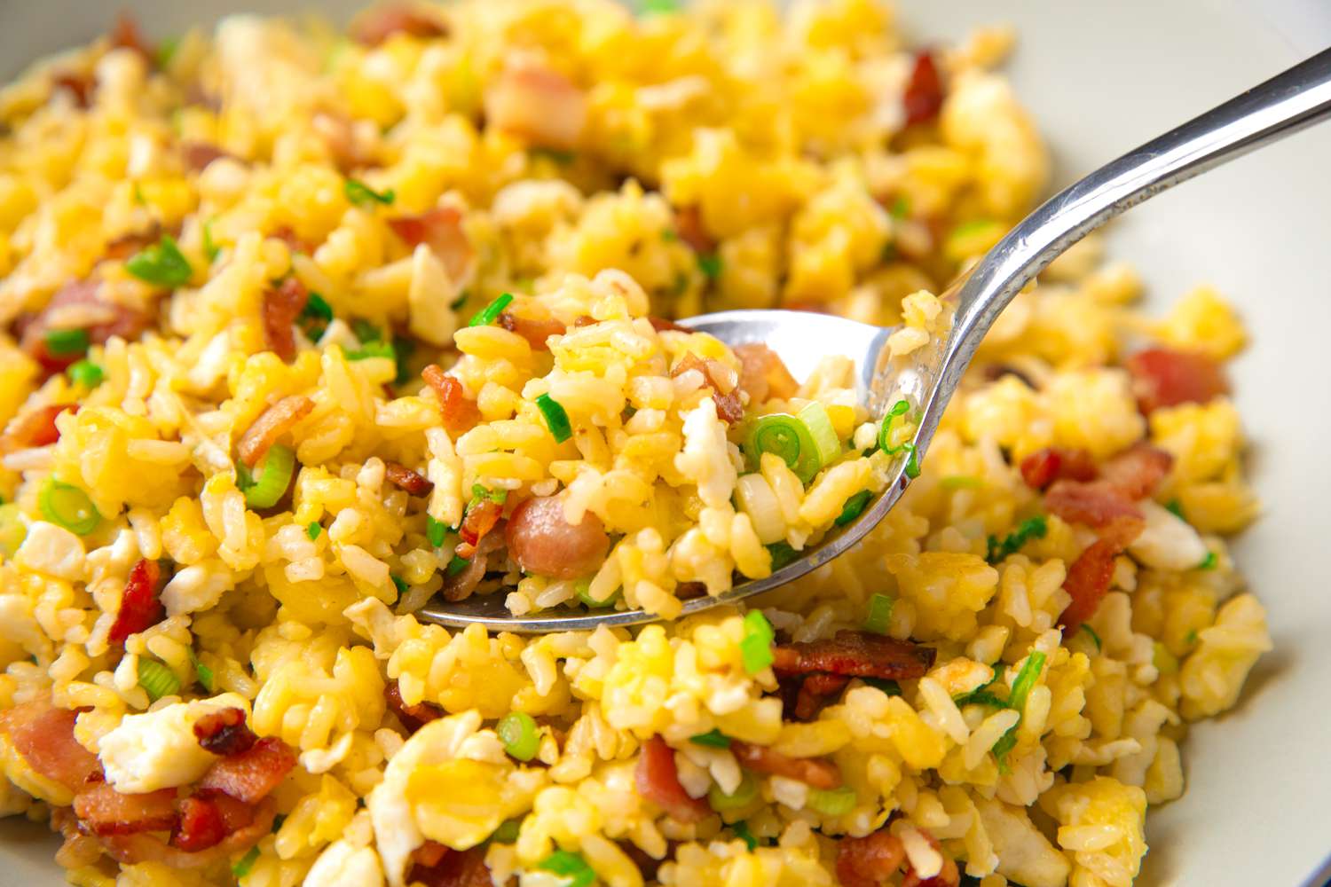 A plate of fried rice with vegetables and diced bacon, served with a spoon