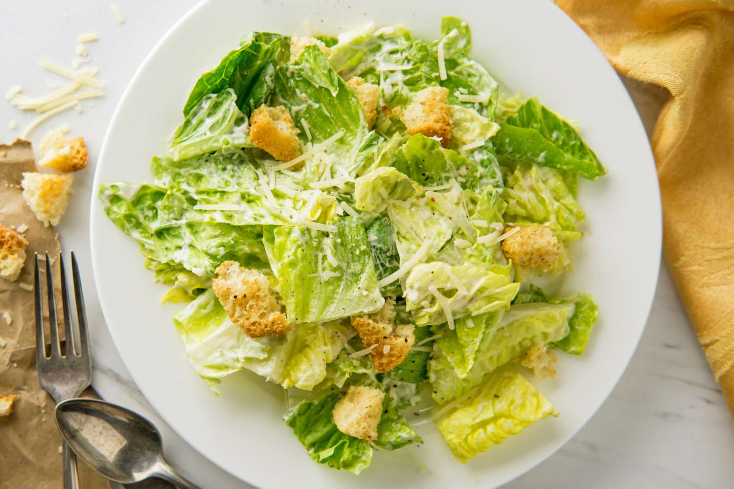 A Caesar salad served on a white plate, featuring romaine lettuce, croutons, grated cheese, and dressing