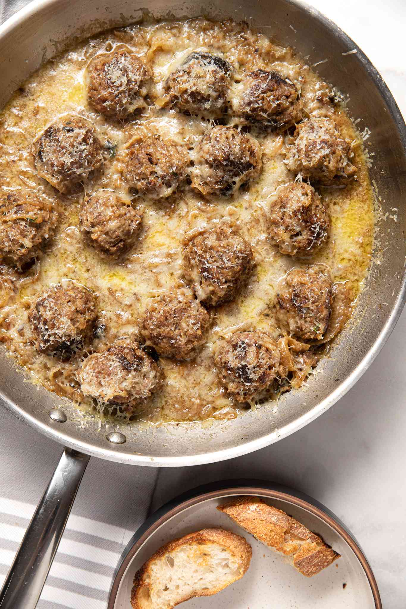 French Onion Meatballs in a Pan, and in Next to It, Toasted Baguette Slices in a Small Bowl