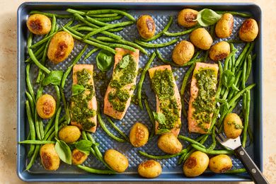A sheetpan with salmon fillets topped with pesto, green beans, potatoes and basil