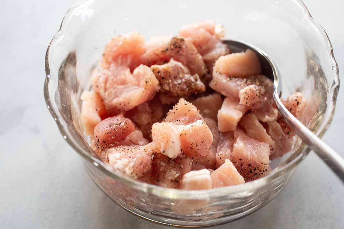 A small glass bowl with chopped raw pork and seasonings inside. A spoon rests inside the bowl.