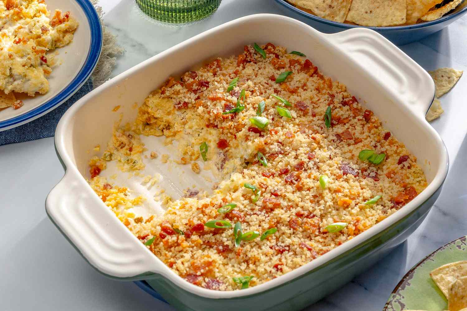 Side view of a square baking dish with jalapeño popper dip, with part of the dip having been scooped out