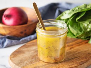 An open jar if Italian dressing on a cutting board with a spoon in it