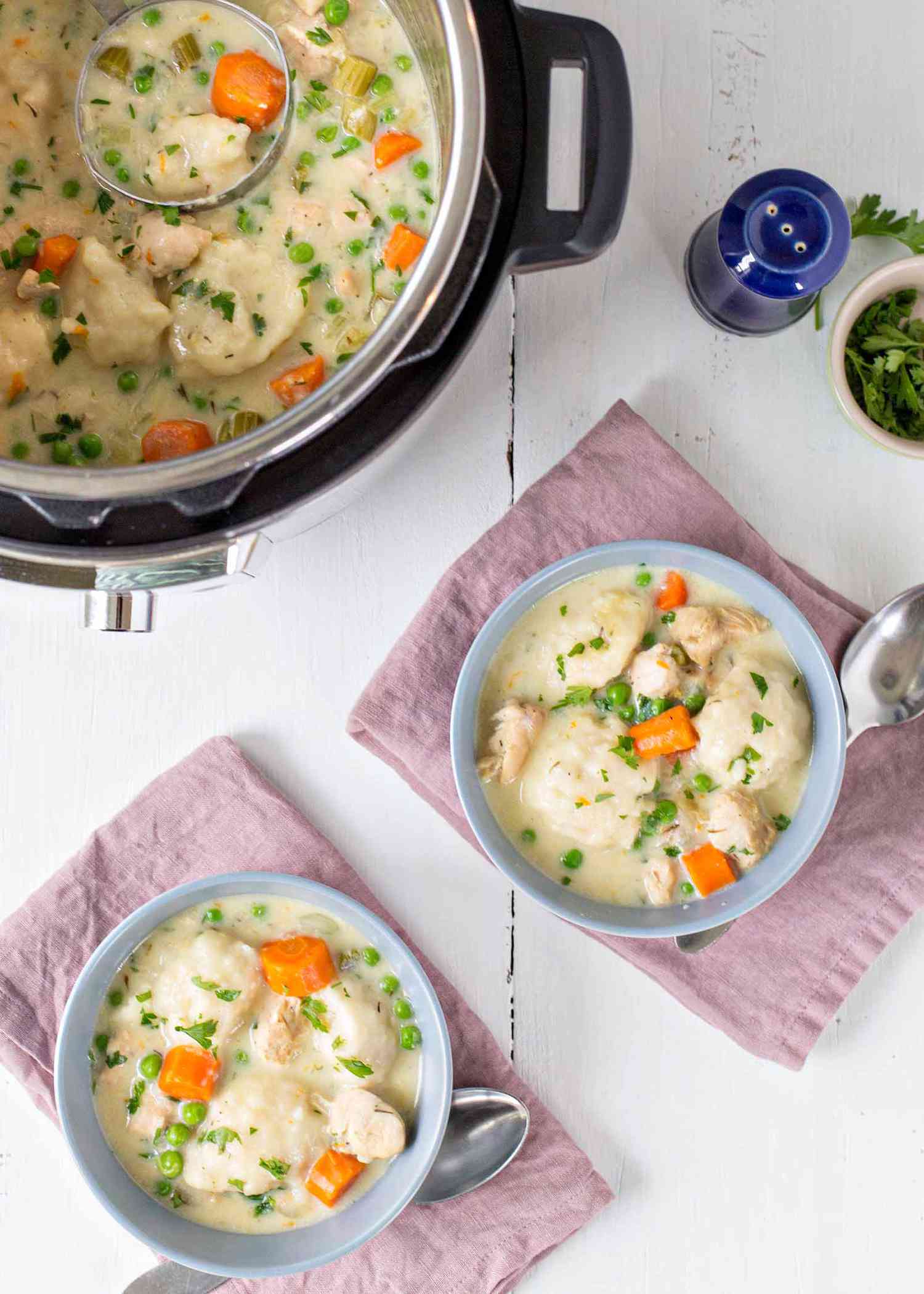 A blue bowl on a pink cloth filled with chicken and dumplings with an instant pot in the background.