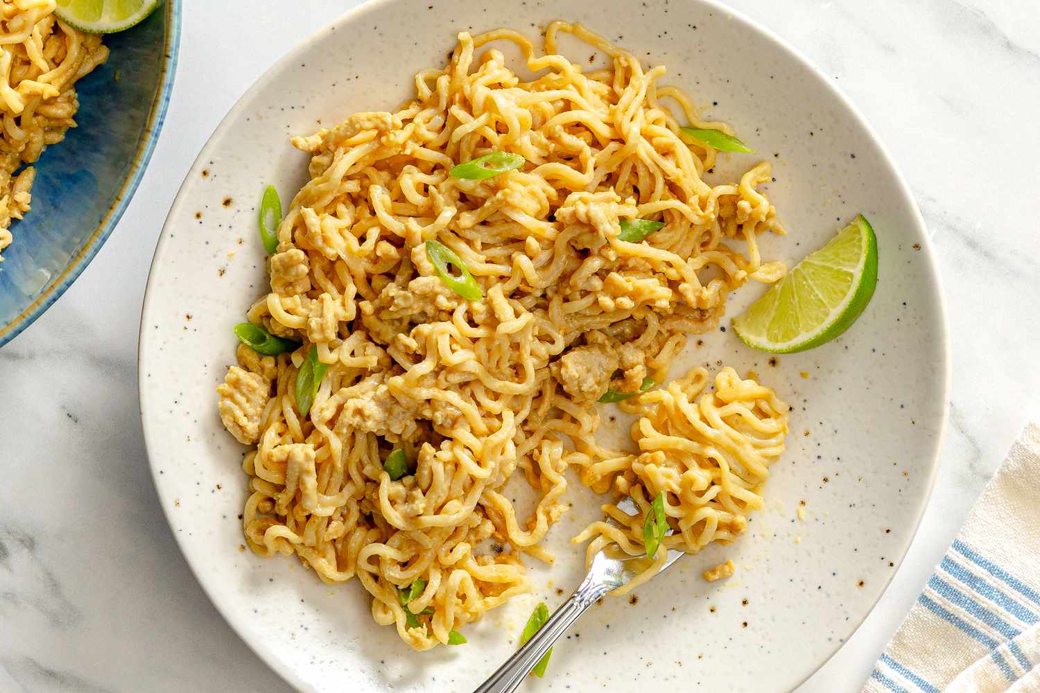 Plate of peanut chicken noodles garnished with a lime wedge