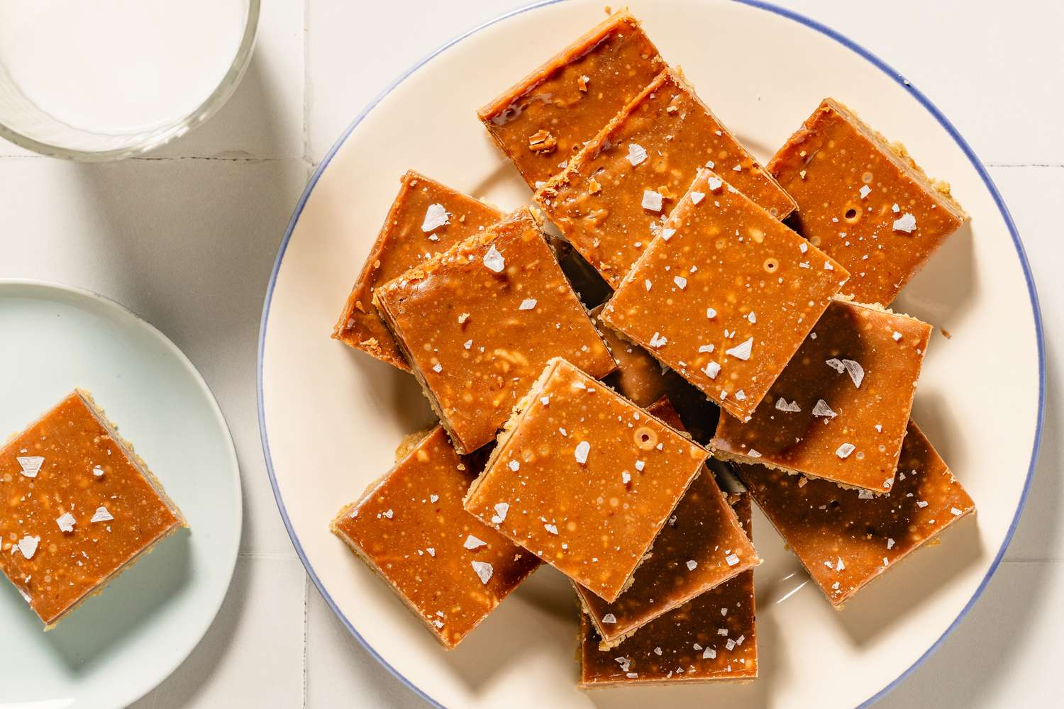A plate of dessert squares topped with a sprinkle of salt arranged neatly on a table near a glass of milk