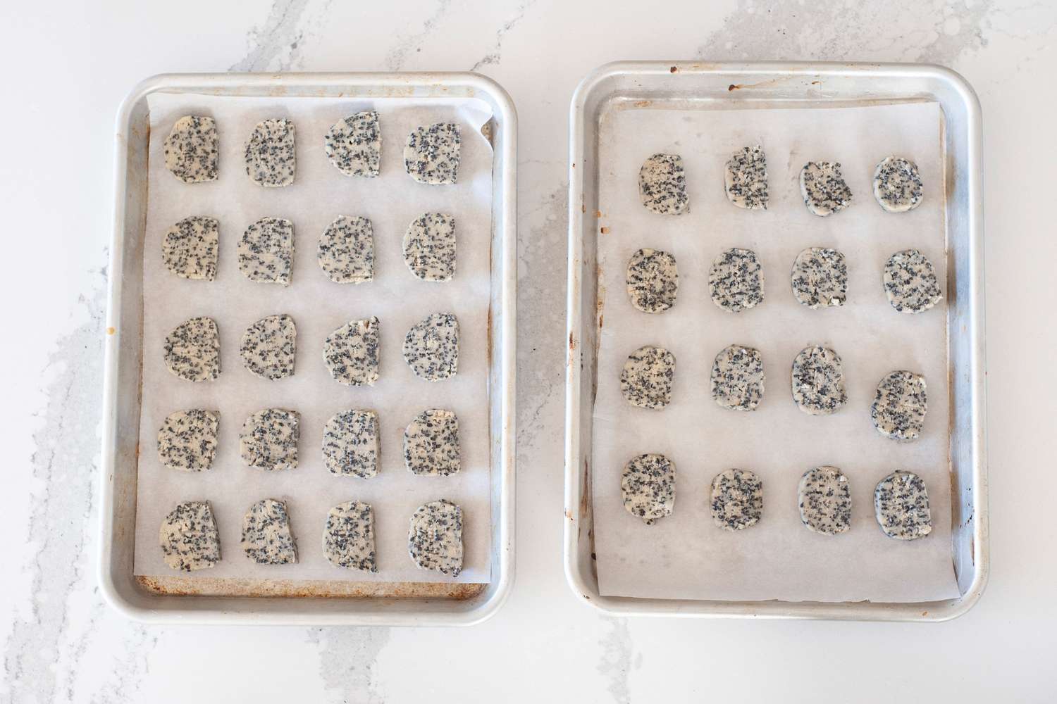 Overhead view of two baking sheets with slice and bake sesame cookies ready for the oven.