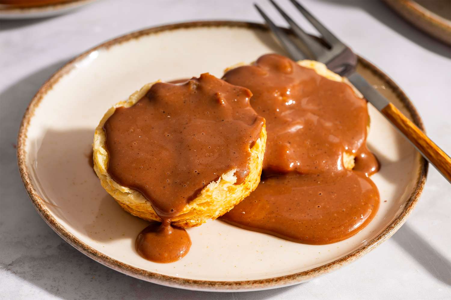 Two biscuits topped with chocolate gravy on a plate with a fork on the side