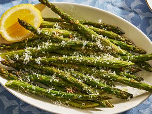 A platter of roasted asparagus garnished with grated Parmesan cheese and half a lemon