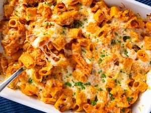 Baked pasta with chicken and cheese served in a white casserole dish topped with chopped chives