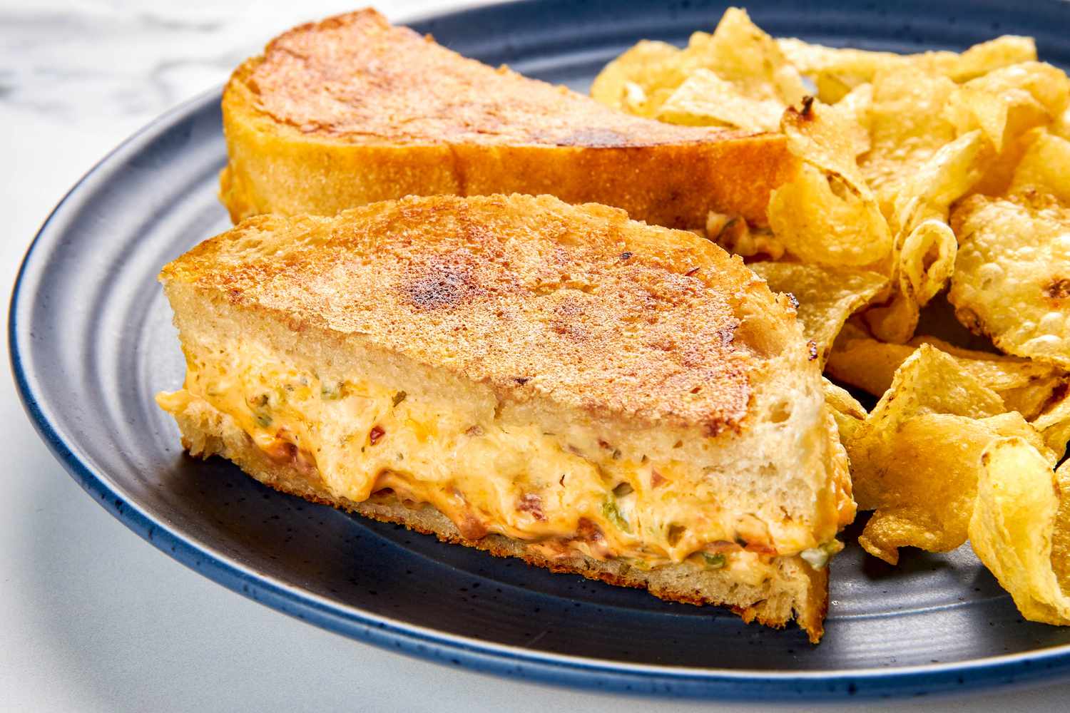 Plate with jalapeno popper grilled cheese (cut in half diagonally and showcasing a cross-section) served with kettle chips
