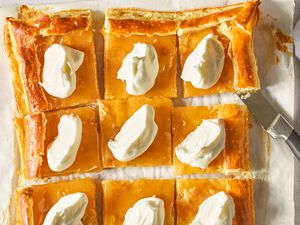 Lemon curd tart cut into squares, each topped with whipped cream.