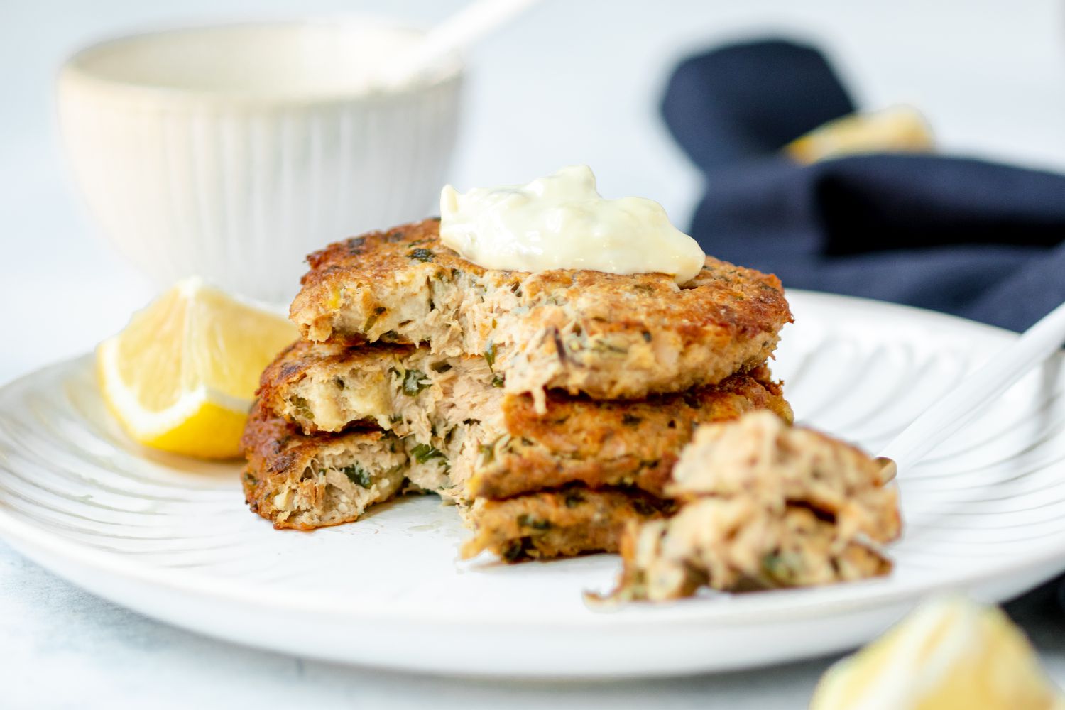 Tuna patties topped with sauce and stacked on a plate with a forkful of patties removed and set next to it.