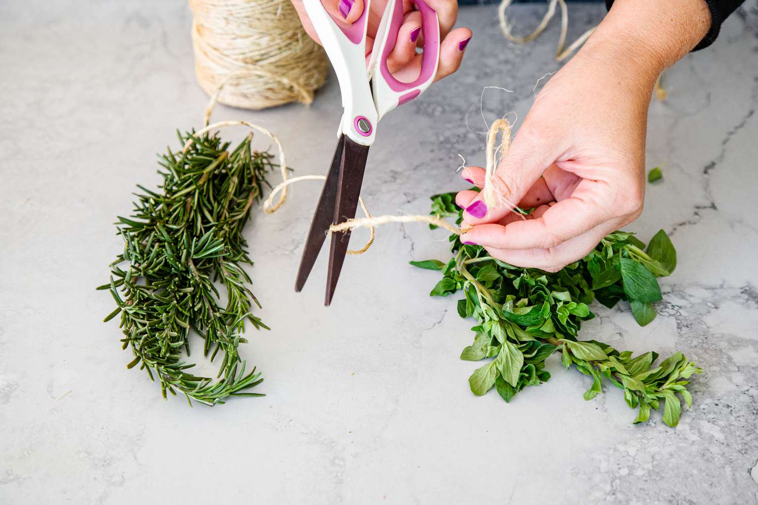 Hands Cutting a Piece of Kitchen Twine and Sprigs of Herbs (Rosemary and Oregano) on the Counter 