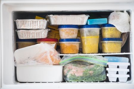 A freezer stocked with various containers and bags of frozen food