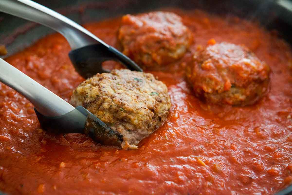 Submerge the italian meatballs in tomato sauce in the skillet