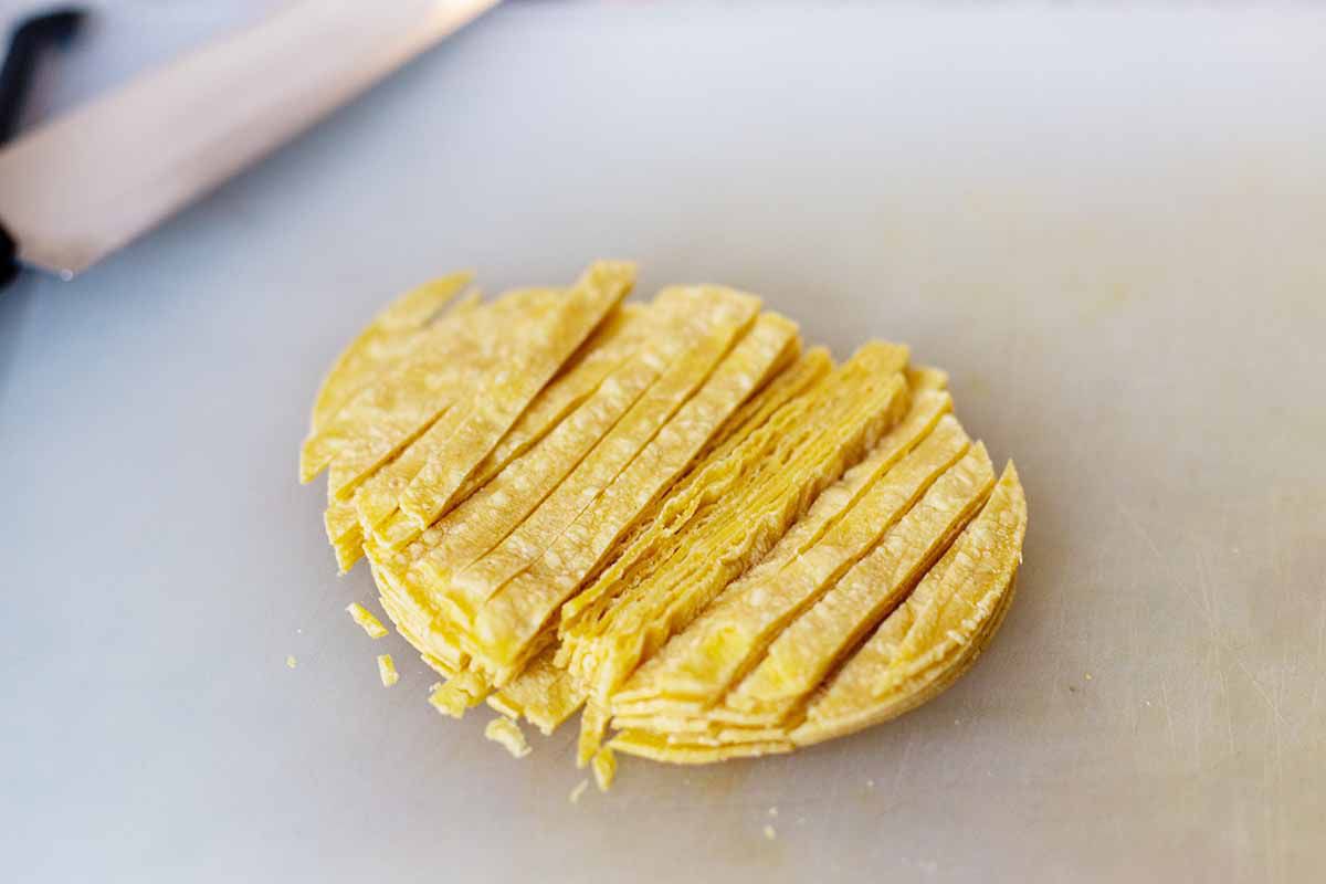 Yellow corn tortillas are stacked and sliced vertically into small strips.
