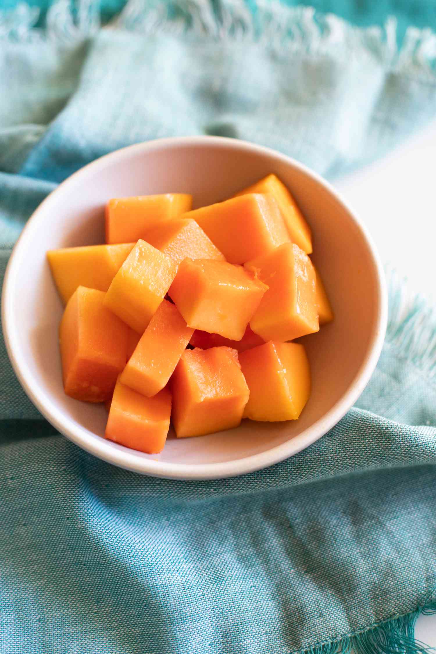 Cut papaya cubes in a white bowl on a blue napkin
