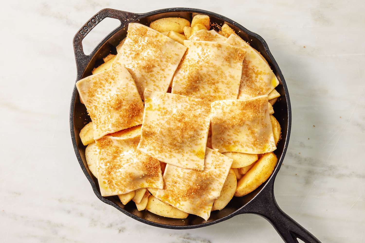 Sliced apples in a skillet topped with squares of pie dough and sprinkled with cinnamon and sugar for the Apple Pandowdy Recipe