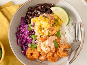 Cajun shrimp bowl with black beans, rice, purple cabbage, and mango salsa with a lime wedge