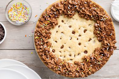 Chocolate Chip Cookie Cake Surrounded by Plates and Small Bowls with Sprinkles and Chocolate Chips