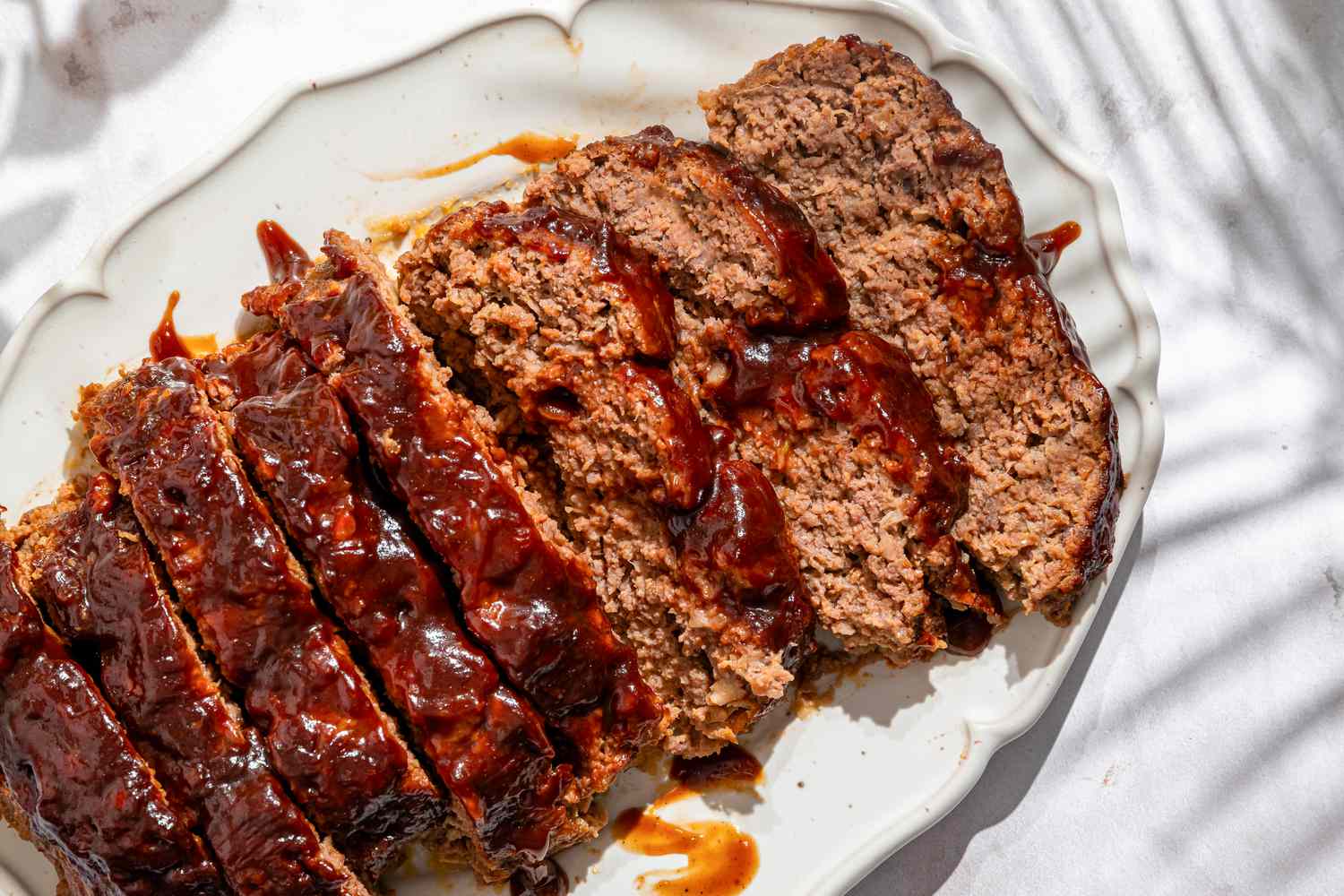 Overhead shot of a sliced up meatloaf on a white serving plate, with three slices turned on their side