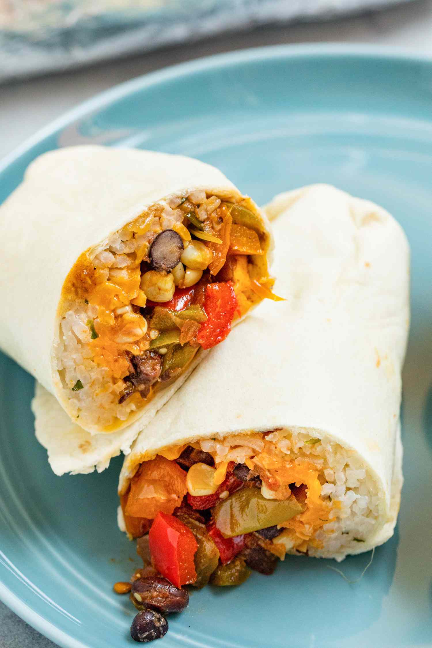 Veggie burritos with beans, corn, and peppers cut in half and set on a plate.