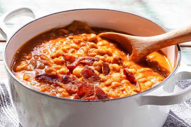 A pot of baked beans with bacon stirred with a wooden spoon
