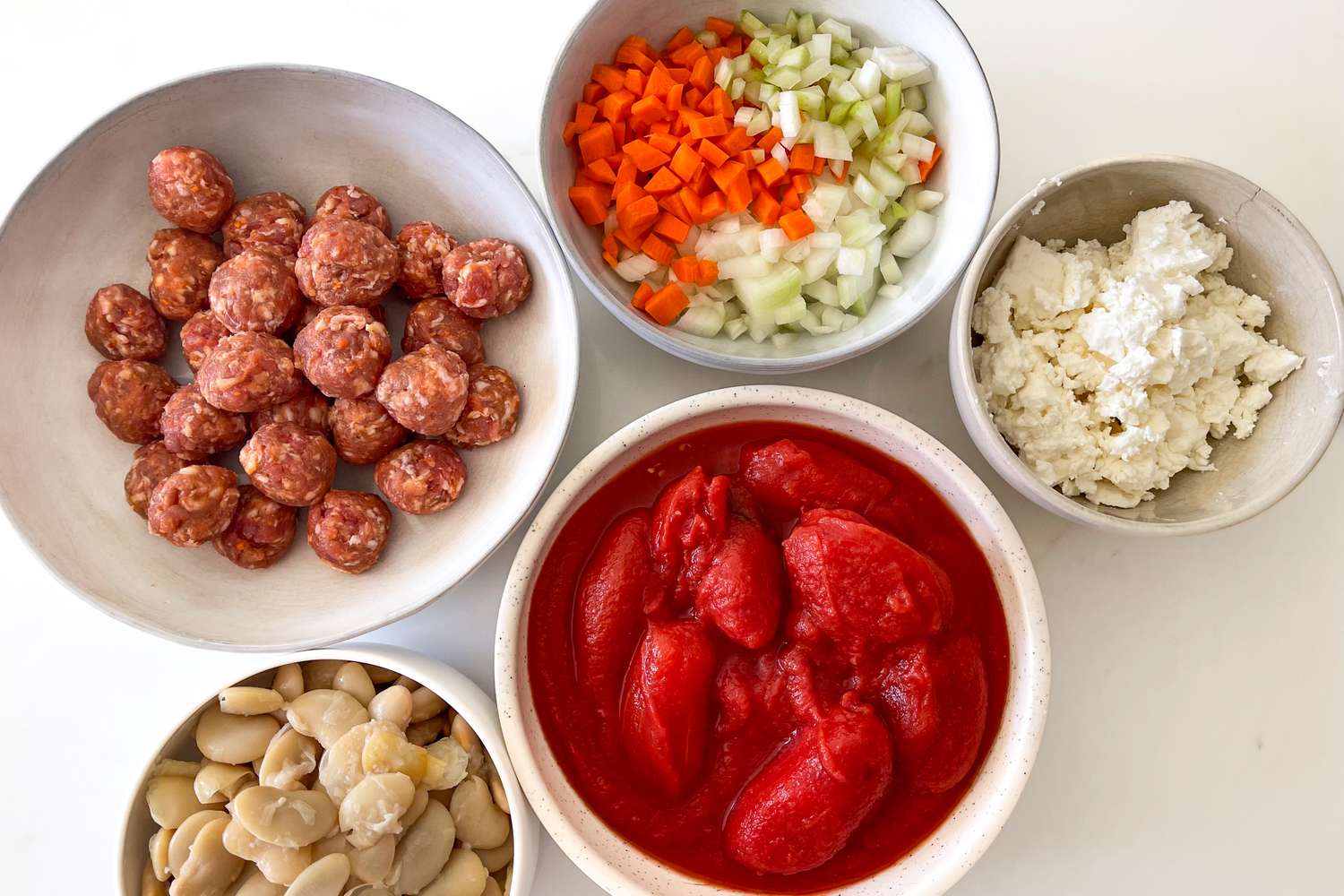 Ingredients in bowls including meatballs chopped vegetables ricotta cheese tomatoes and beans