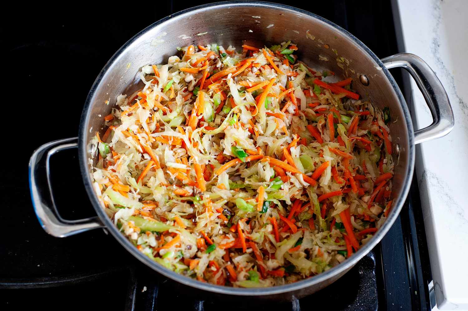 Making the filling for fried egg rolls with cabbage, carrots, and mushrooms in a large pot.