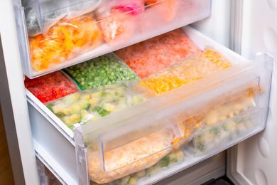 Plastic bags with different frozen vegetables in open refrigerator drawer