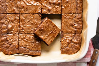Overhead view of a white baking dish of brownies on parchment paper, sliced into squares with one slice removed