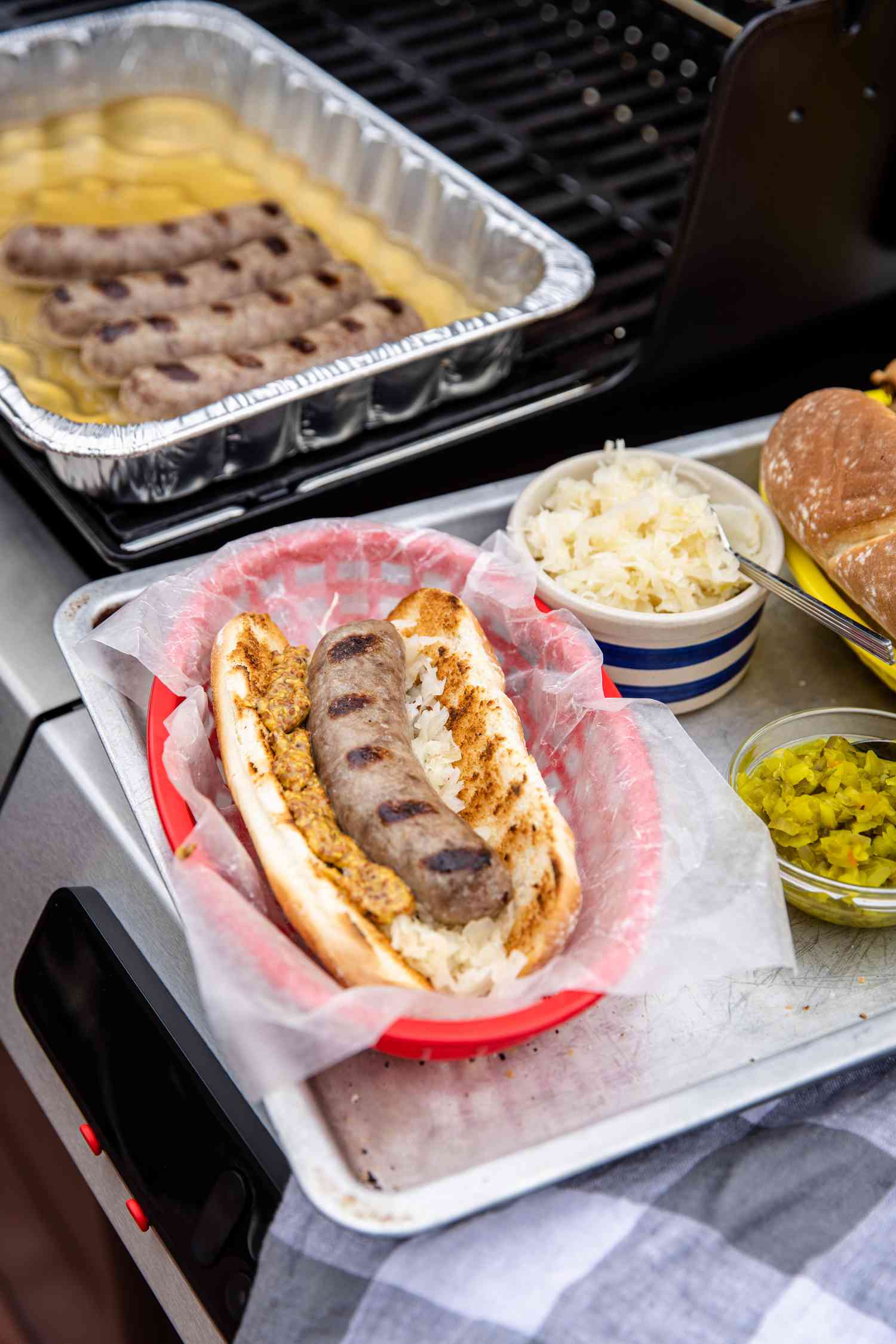Beer Brats Topped with Sauerkraut and Mustard Next to Bowls with Sauerkraut and Relish